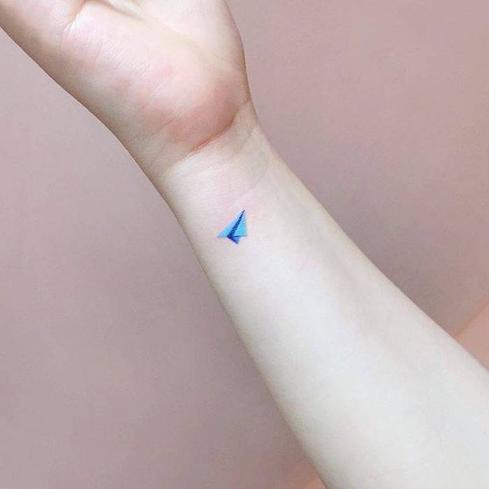 Mini Tattoo Ideen zum Inspirieren, farbiges Papierflieger Tattoo am Handgelenk, blauer Papierflieger 