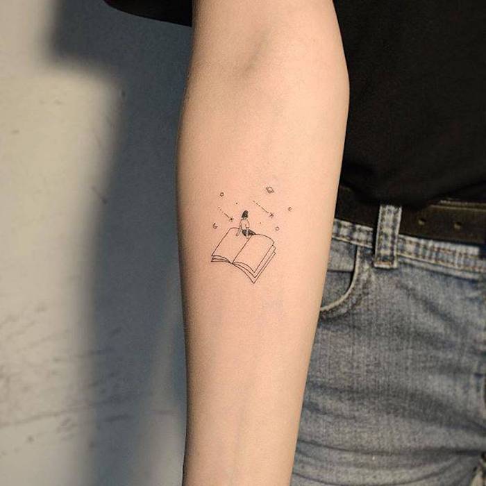 Kleines Tattoo am Unterarm, Frau sitzend auf geöffnetem Buch, kleine Sterne und Planeten 
