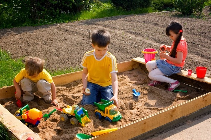 sandkasten-selber-bauen-glueckliche-Kinder-spielen-in-einem-Sandkasten
