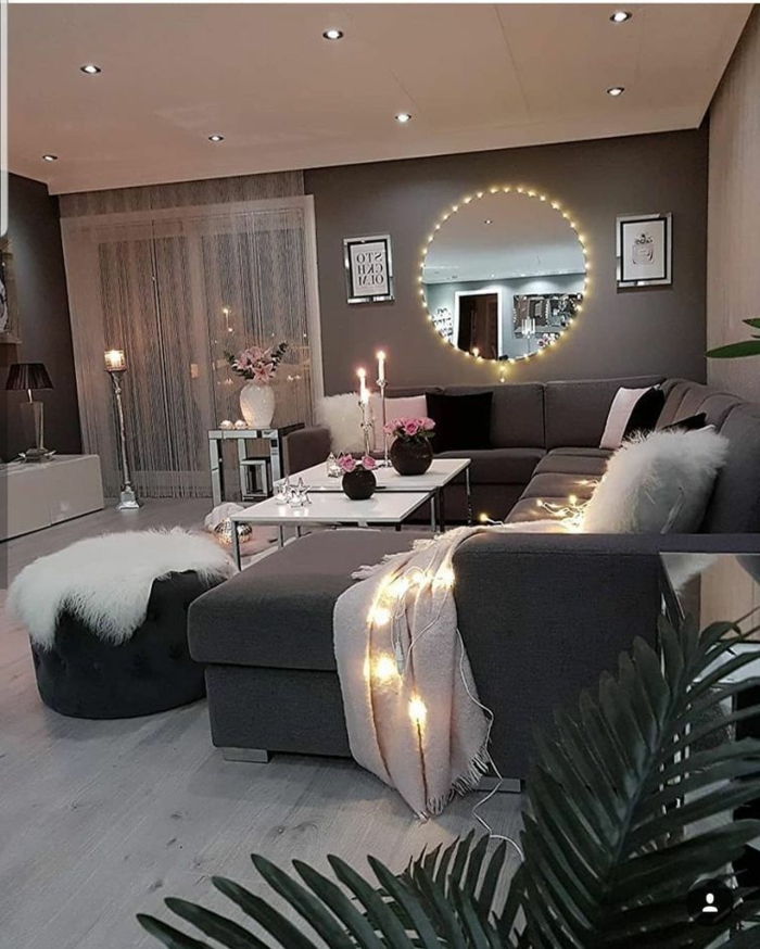 romantische und gemütliche Inneneinrichtung mit kleinen Lichtern, großes Sofa, runder Spiegel, Wohnzimmer gestalten