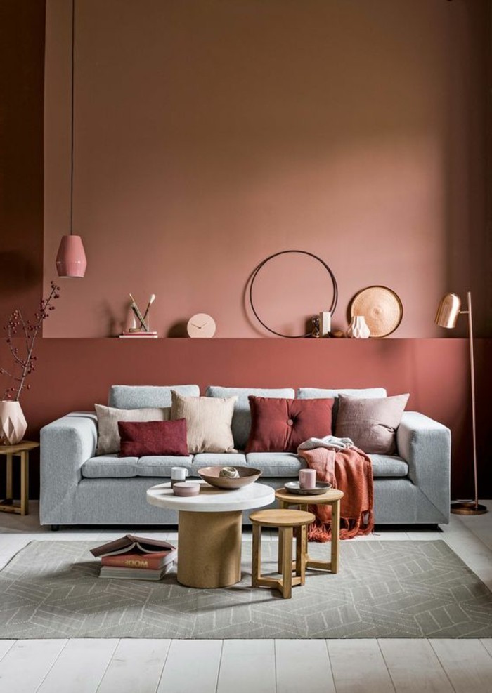 farbgestaltung-waende-ziegelrot-stehlampe-gold-wanduhr-hellgraue-couch-runder-holztisch-musterteppich-ikebana-vase