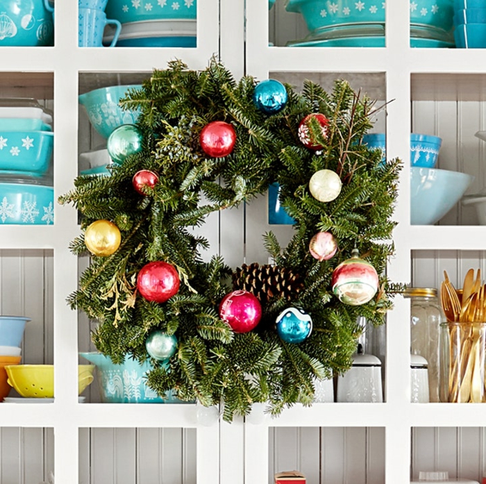 traditionellen kranz weihnachten inspiration grüner weihnachtskranz dekoriert mit bunten weihnachtskugeln und tannenzapfen weißer küchenschrank