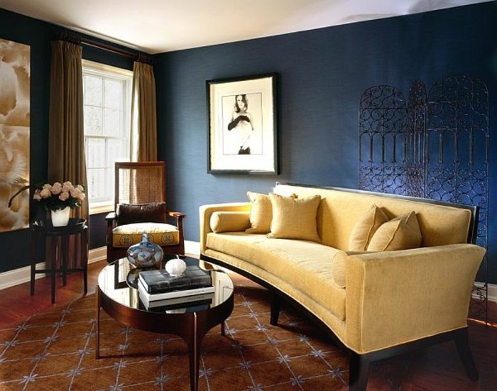 wandfarbe-blau-farbgestaltung-waende-farbige-waende-hellgelbe-couch-kissen-musterteppich-holzboden-holzstuhl-ovaler-tisch-glas-dekorative-vase