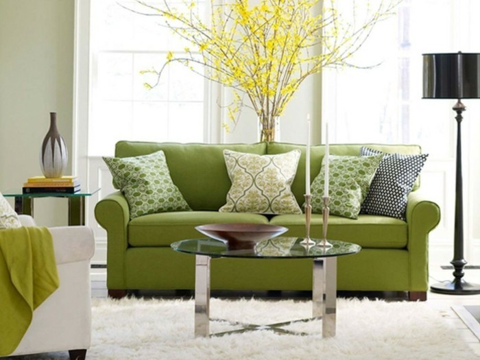1farbgestaltung-wohnzimmer-couch-in-gruen-kissen-musterbezuege-gelbe-pflanze-weisser-teppich-runder-glastisch-kerzen-sessel-weiss-stehlampe-vase