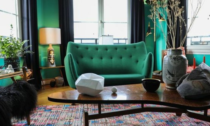 3feng-shui-farben-farbgestaltung-wohnzimmer-gruene-couch-gruene-wand-schwarze-gardinen-bunter-teppich-ovaler-holztisch-tischdeko-vase-indirektes-licht