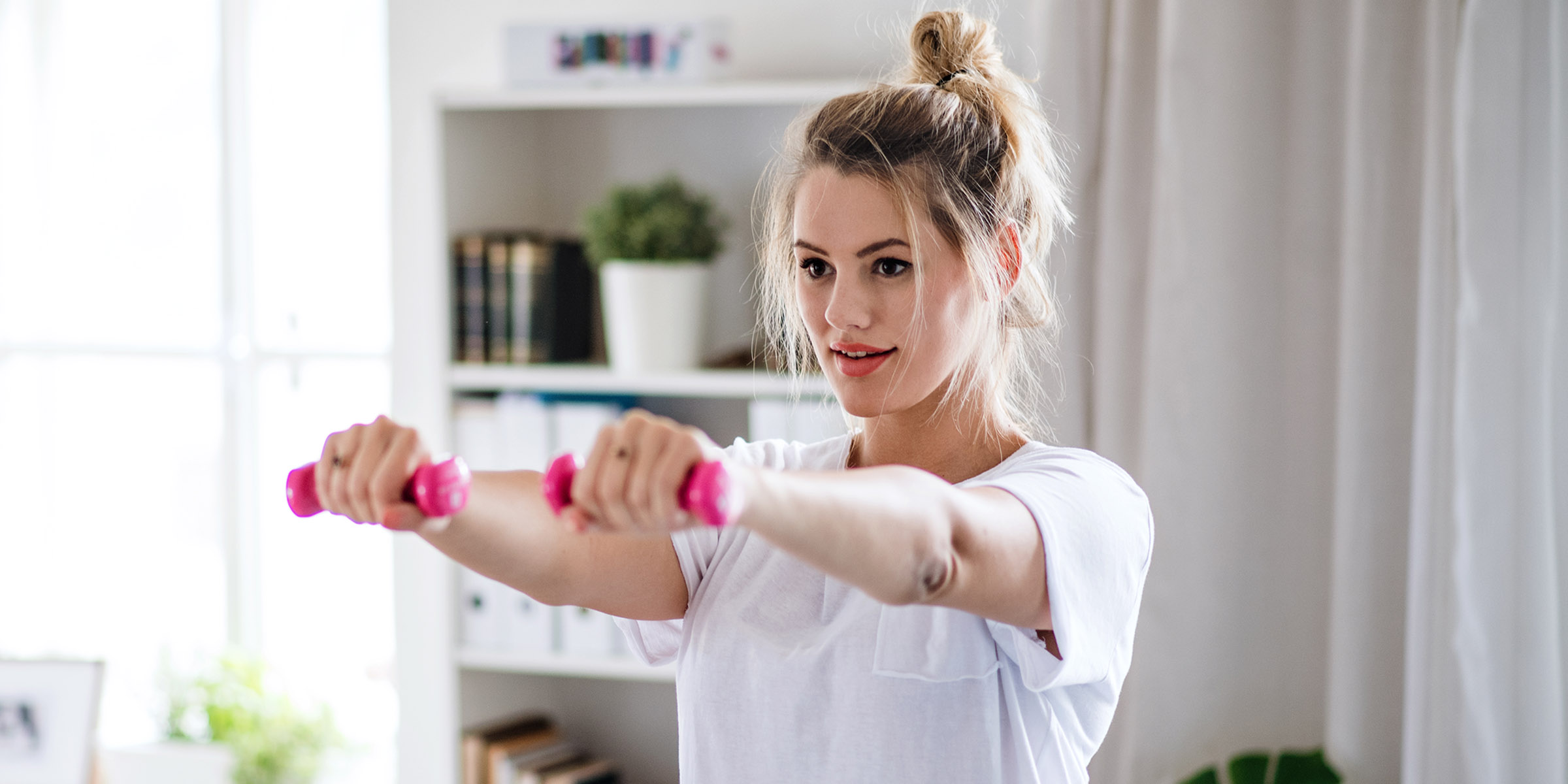 young woman with dumbbells doing exercise in bedroom indoors at home.