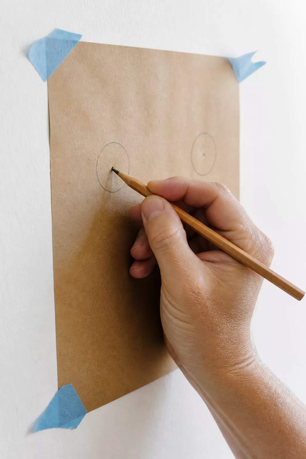 Hand markiert den Bohrpunkt auf der an der Wand fixierten Papierschablone