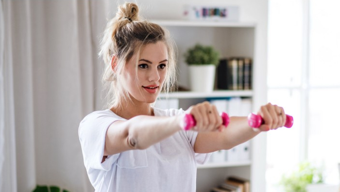 young woman with dumbbells doing exercise in bedroom indoors at home.