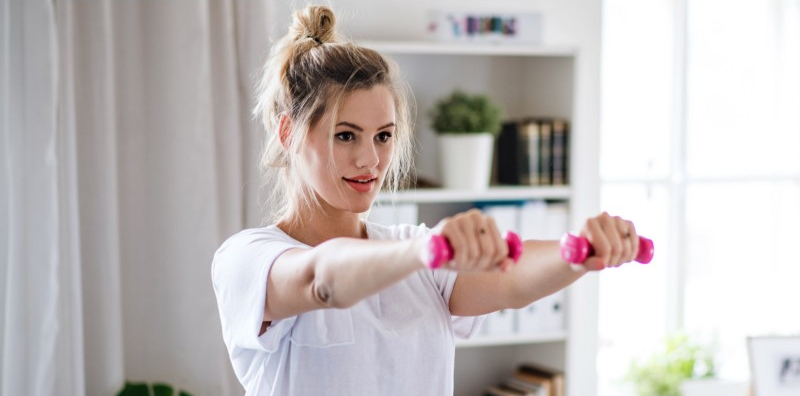 young woman with dumbbells doing exercise in bedroom indoors at home.