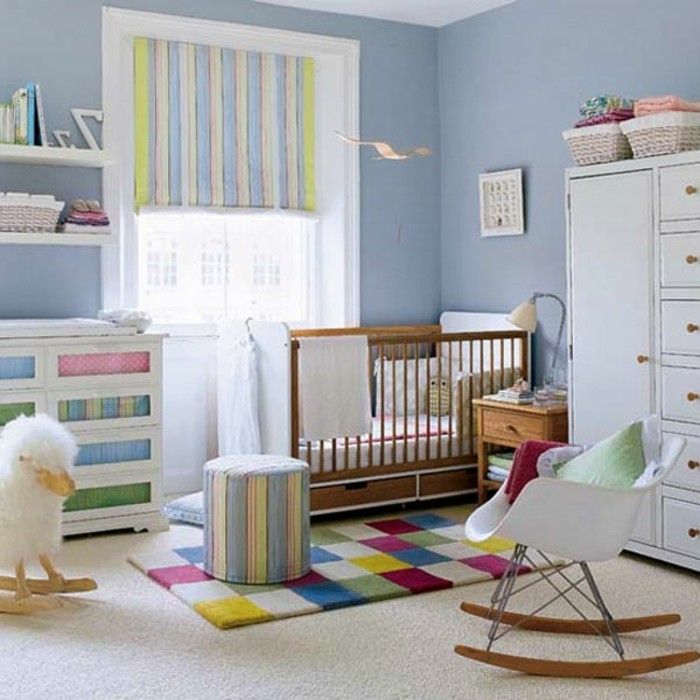 babyzimmer-tapete-blau-bunter-teppich-rollos-schaukelstuhl-holzbeine-plastiksitz-weißer-schrank