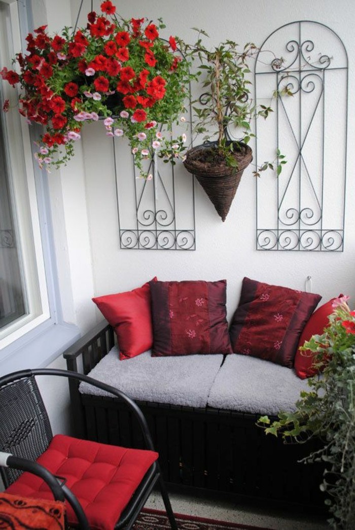 ideen-kleiner-balkon-wanddeko-rote-blumen-kleiner-sofa-dekokissen-geflochtener-stuhl
