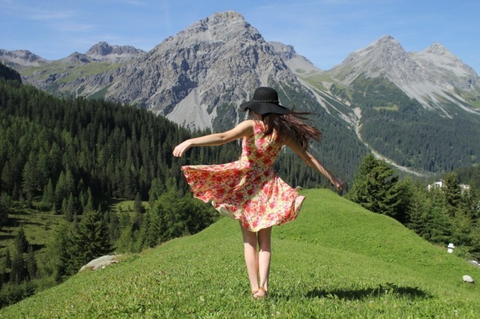 reiselustige-frau-gebirge-schoene-natur-naturfreunde-tanzen-buntes-kleid-lange-haare