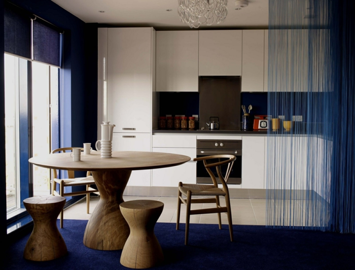 offene-küche-wohnzimmer-abtrennen-runder-esstisch-massivholz-holzstühle-blauer-plüschteppich-rollos