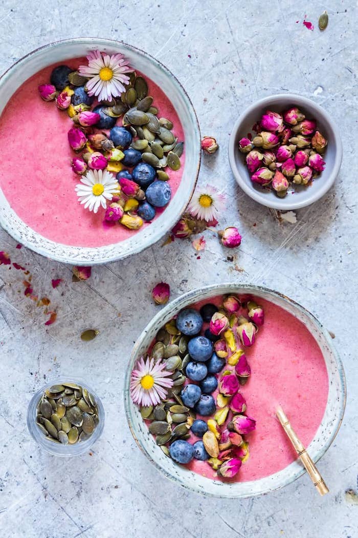 Pink Smoothie Rezept, dekoriert mit Blaubeeren Kürbissamen und essbaren Blüten, gesundes Frühstück Ideen 