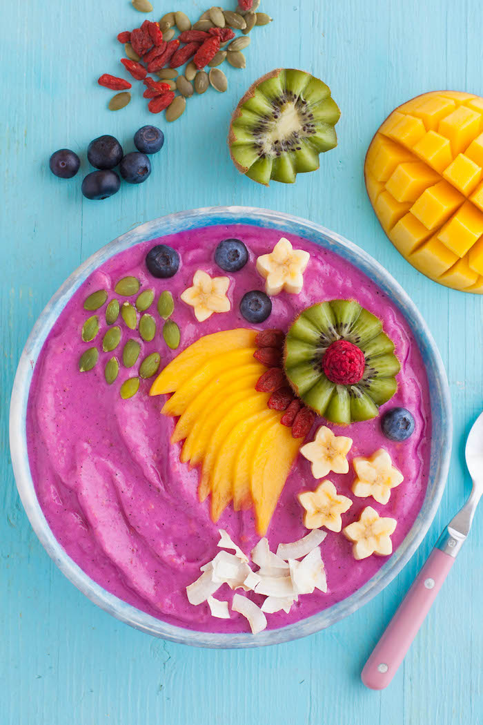 Violett Smoothie Bowl, dekoriert mit Mango Sternfrüchten Kiwi Blaubeeren Goji Beeren und Kokos 