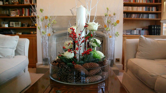 eine saisonale Deko mit Zapfen, weißen Rosen, roten Beeren und einer großen weißen Kerze