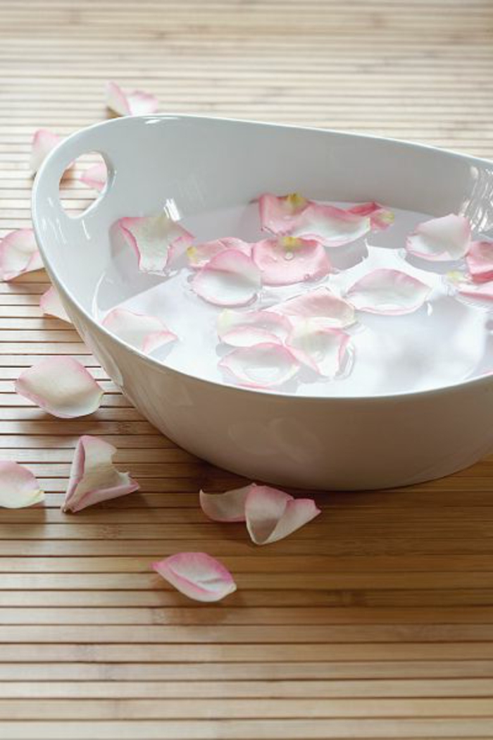 eine weiße Schüssel mit kaltem Wasser und hellpinken Rosenblättern für Anti-Falten-Therapie und kleine Poren