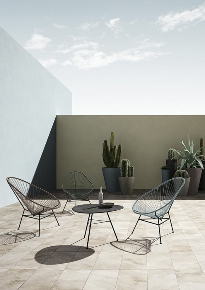 Dachterrasse im minimalistischen Stil mit drei Metallstühlen und einem schwarzen Kaffeetisch, riesengroße Kakteen