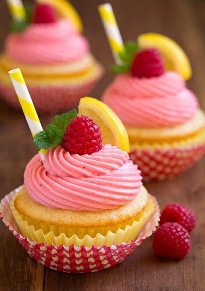 kleine muffins dekoriert mit rosa sahne, himbeeren, pfefferminze und zitrone