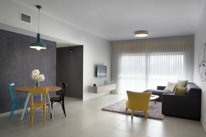 Wohnzimmer mit hellen Bodenfliesen, runder Esstisch aus Holz, 3-Stuhl-Set, schwarze Eckcouch, Fernseher