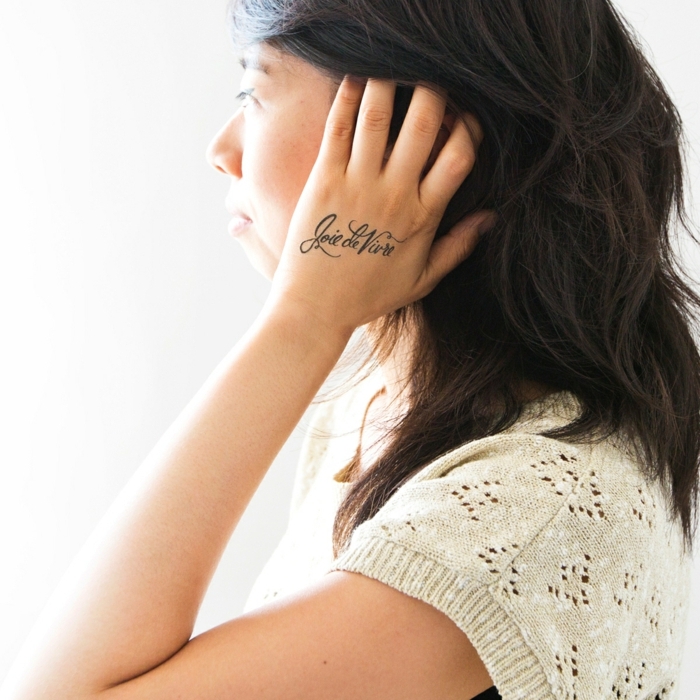 tattoo motive dezente idee für frauen schrift auf der hand schwarze haare spitze gestrickte bluse