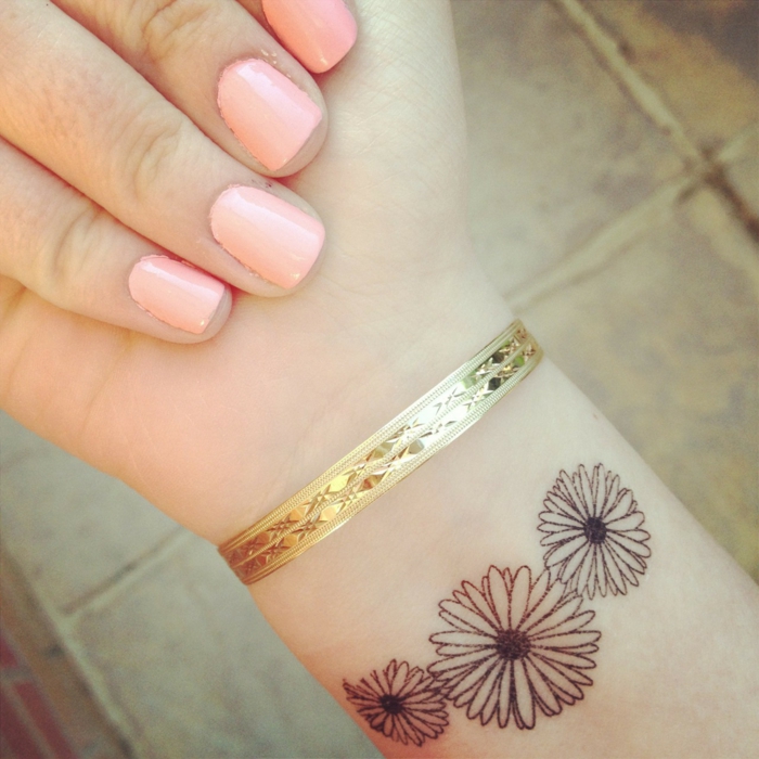 dezentes tattoo gestaltet in form von drei schönen kleinen blumen goldenes armband tolle maniküre