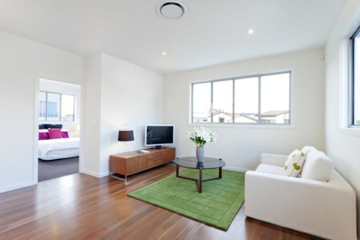 weiß gestrichene Wohnung mit Laminatboden, grüner Teppich, runder Designer-Couchtisch, weiße Couch