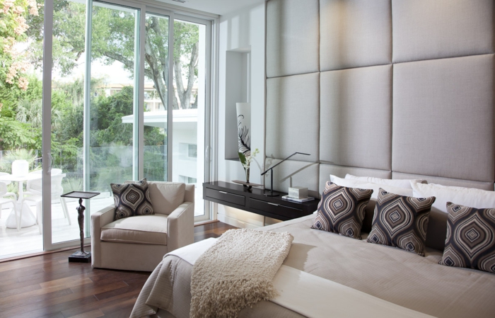 Wandverkleidung, Doppelbett mit Musterkissen, weißer Sessel mit Beistelltisch, Terrasse mit Schiebetür
