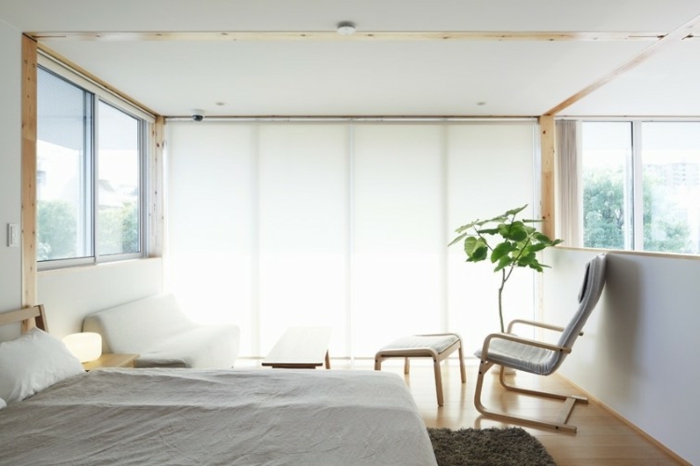 Schlafzimmer mit weißer Couch, Relax-Stuhl mit weißer Hocker, Doppelbett mit weißer Schlafdecke