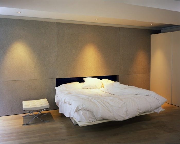 minimalistisches Schlafzimmer in Naturfarben mit Doppelbett mit weißen Lacken, Lederhocker in Weiß, Led-Licht
