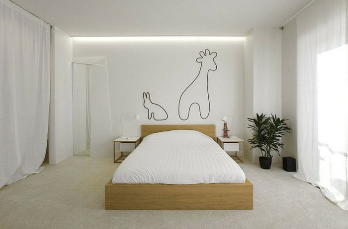 weiß gestrichenes Schlafzimmer mit Holzbett, langen weißen Gardinen und einfachen Zeichnungen an der Wand