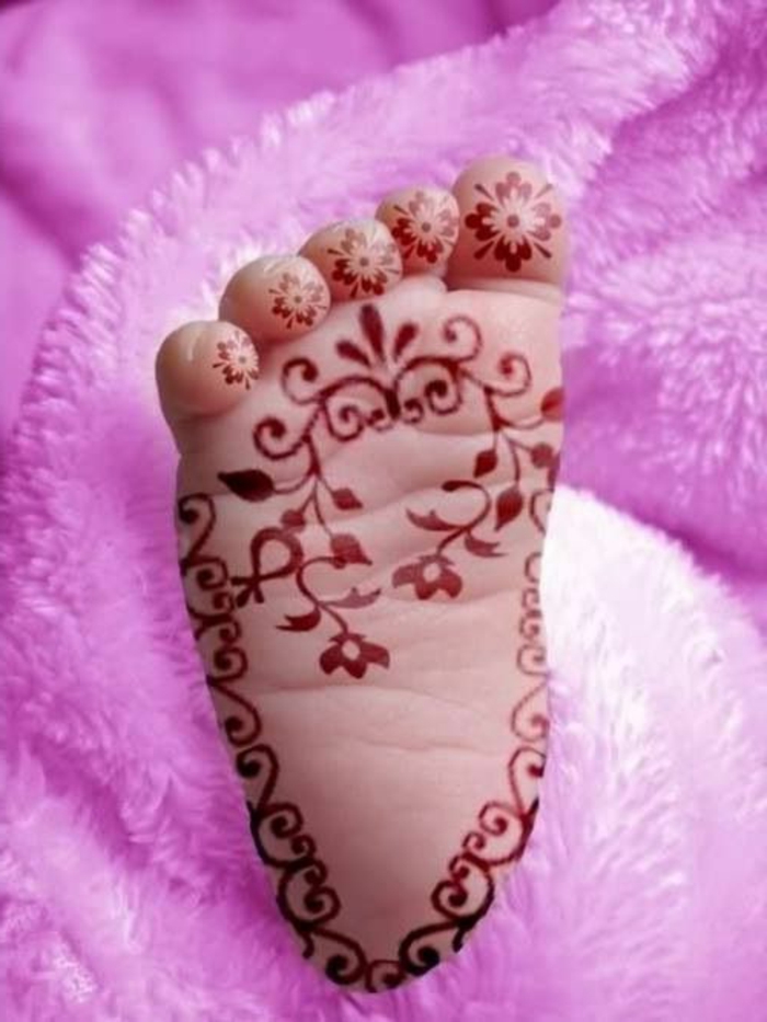ein Babyfuß mit Tattoo aus roter Henna Farbe, Zehentattoo für Babys, florale Motive, pinke Plüschdecke