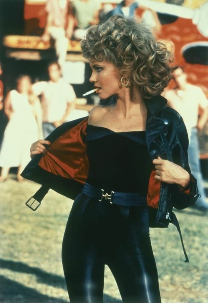 Olivia Newton Johns 80er Jahre Outfit mit Lederhose in Schwart, schwarzer schulterfreien Bluse und schwarzer Lederjacke