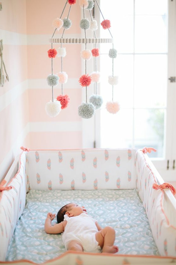 babyzimmer grau rosa spielzeug fliegt über dem baby bunte fell bälle deko schlafendes baby