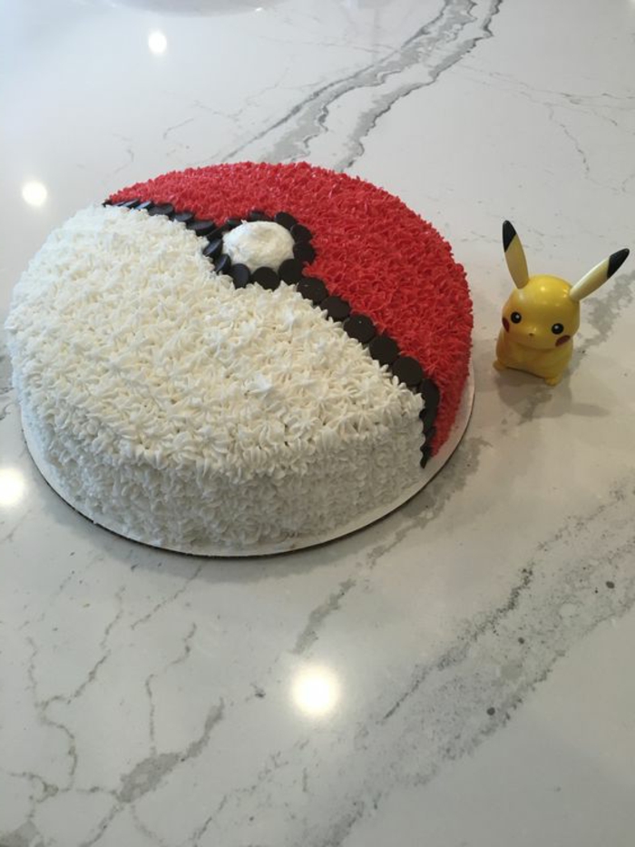 leckere pokemon torte, die wie in pokeball ausseieht - mit schwarzer, weißer und roter creme, und ein kleines gelbes pikachu 