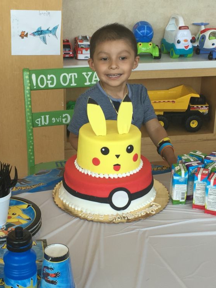 hier ist kind mit einer zweistöckigen torte - ein gelbes pokemon wesen pikachu und ein roter pokeball