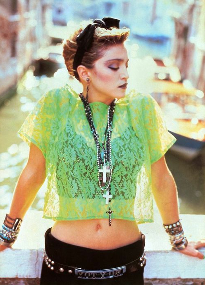 Madonna in den 80er Jahren mit einer grünen Tüllbluse, schwarzem Haarband, schwarzer Hose und vielen Armbändern