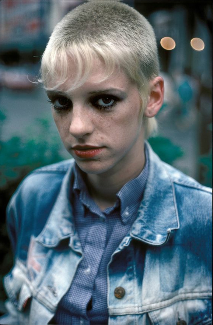 ein Punk-Mädchen mit blonden Haaren - vorne lang, oben kurz, gewaschene Jacke, blaues Hemd