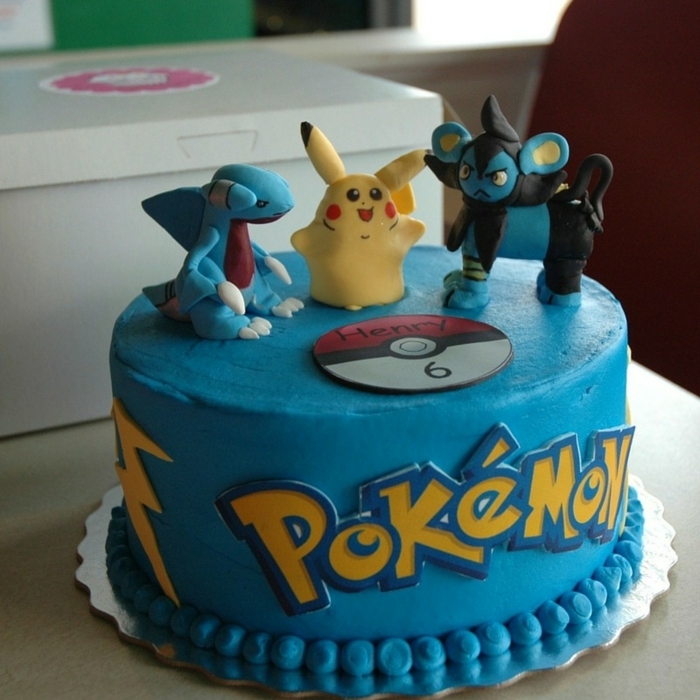 eine blaue pokemon torte mit einem roten pokeball und drei kleinen pokemon wesen und eine gelbe überschrift 