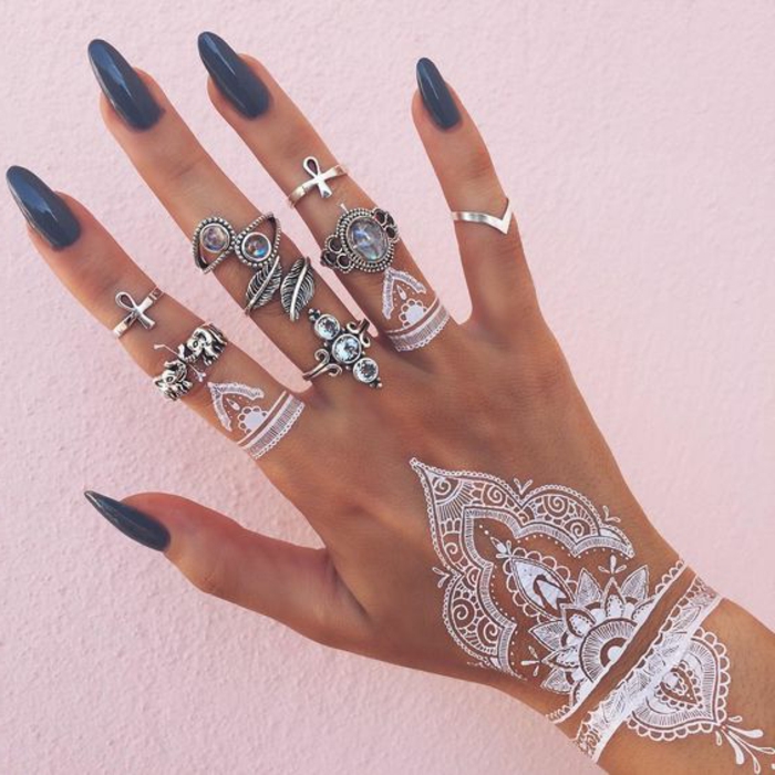 eine Hand mit vielen Ringen aus Silber, weiße Fingertattoos, Handoberflächentattoo aus weißem Henna