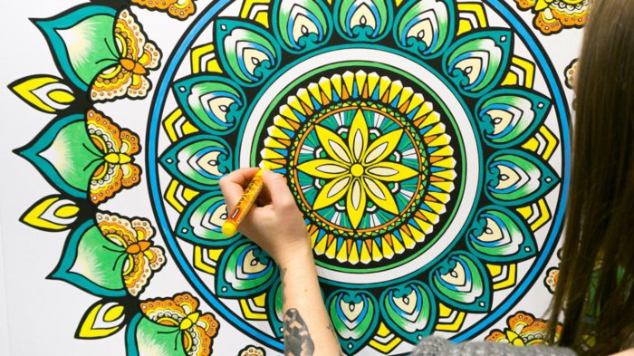 ein Mädchen malt ein riesiges Mandala mit Farbstiften aus, Schmetterlinge malen, Gelb, Orange, Blau, Grün