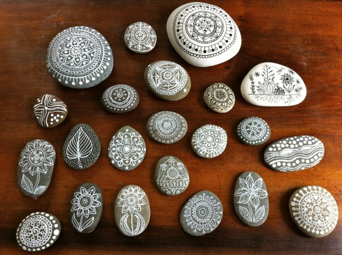 weiße und graue Steine mit Mandala-Zeichnungen bemalen, große und kleine Steine, Holztisch