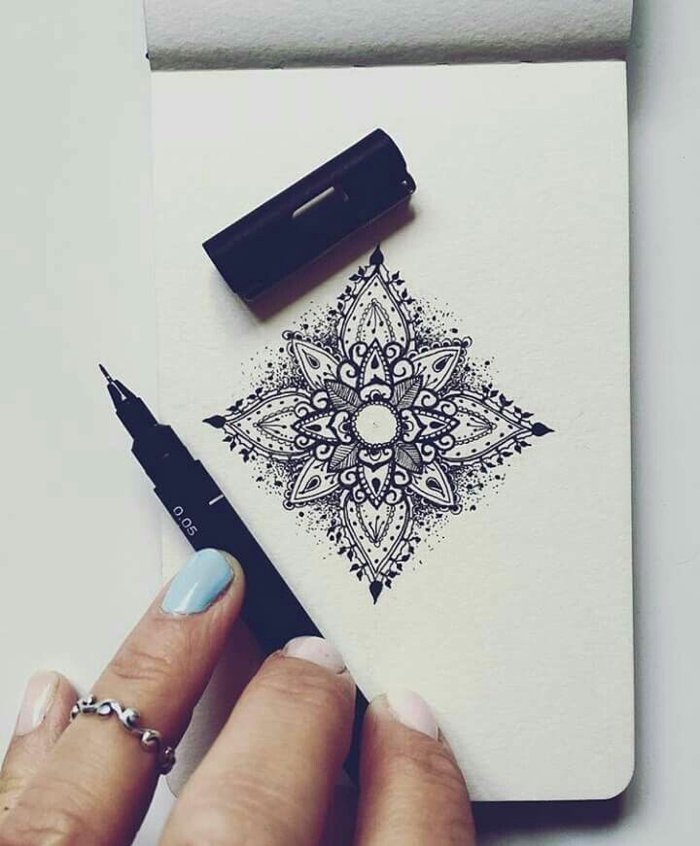 kleines Notizbuch, kleine Mandalas in viereckiger Form, schwarzer Stift, Frauenhand, lackierte Nägel