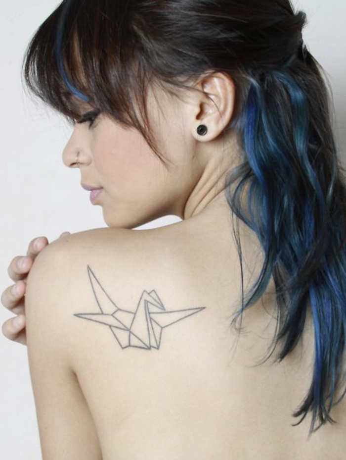 hier ist eine junge frau mit einem blauen haar und mit einem kleinen origami tattoo auf dem schulterblatt - eine weiße fliegende origami taube 