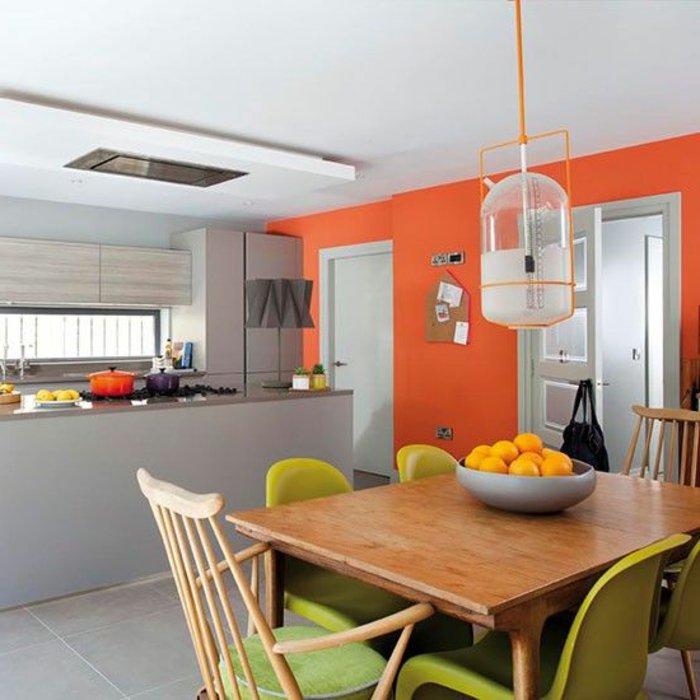 orange Wände, grüne Stühle, weiße Lampe aus Glas, graue Theke, perlgraue Küche