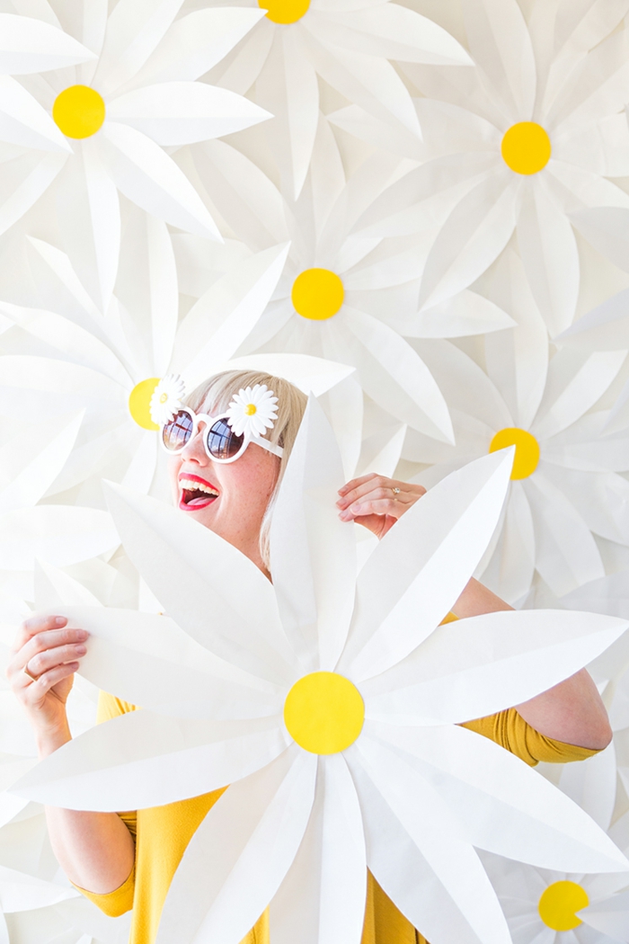 wanddeko aus papier, papierblumen, gänseblumen, diy, frau mit blonen haaren und sonnnenbrillen