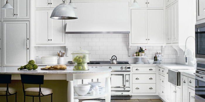 weiße Küche mit Marmor-Kochinsel, vielen Schränken in weißer Farbe und runden Metallgriffen