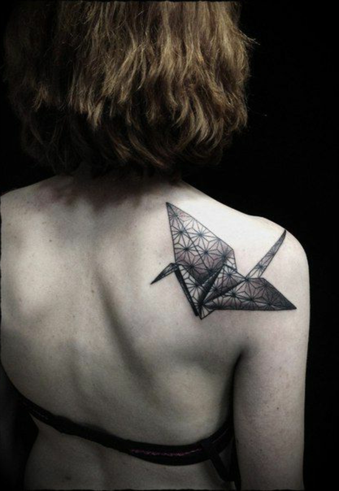 werfen sie einen blick auf diese idee für einen origami tattoo - ein kleiner schwarzer origami vogel auf dem schulterblatt einer jungen frau 