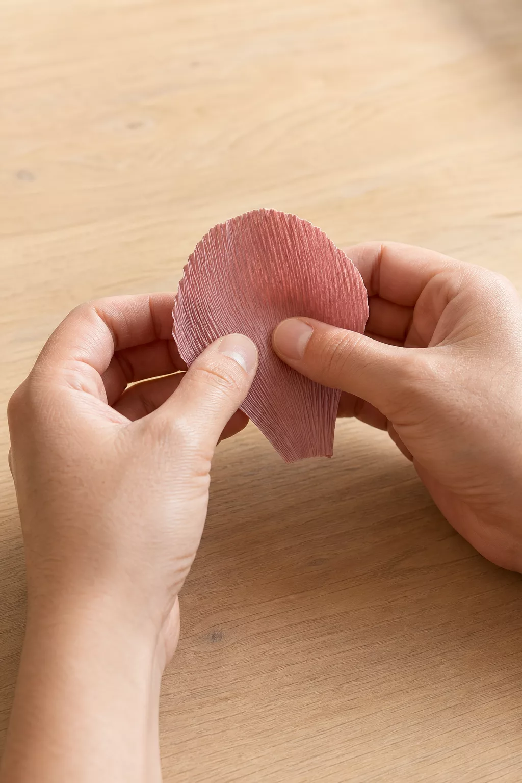 Hände dehnen ein Krepppapier-Blütenblatt, Rillen sichtbar