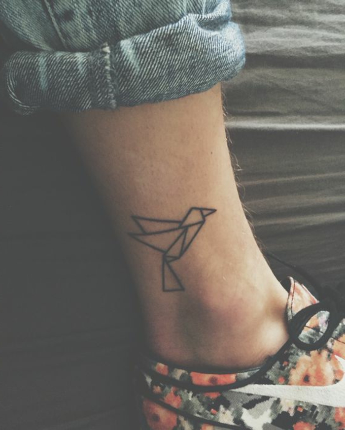ein bein mit einem winzigen mini tattoo mit origami motiven - ein kleiner schwarzer fliegender origami vogel 